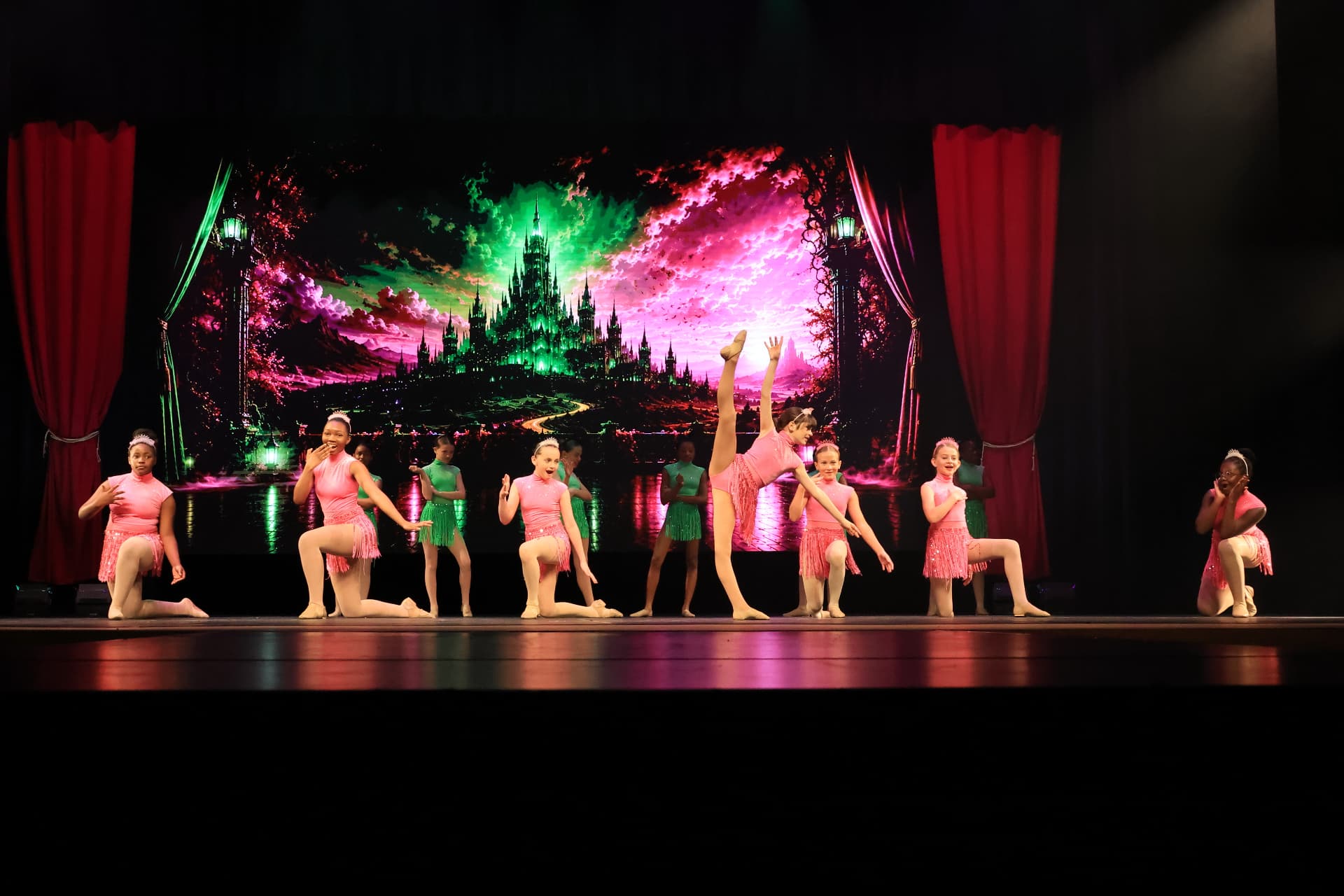 Company dancers kneeling on stage in pink and green fringe costumes