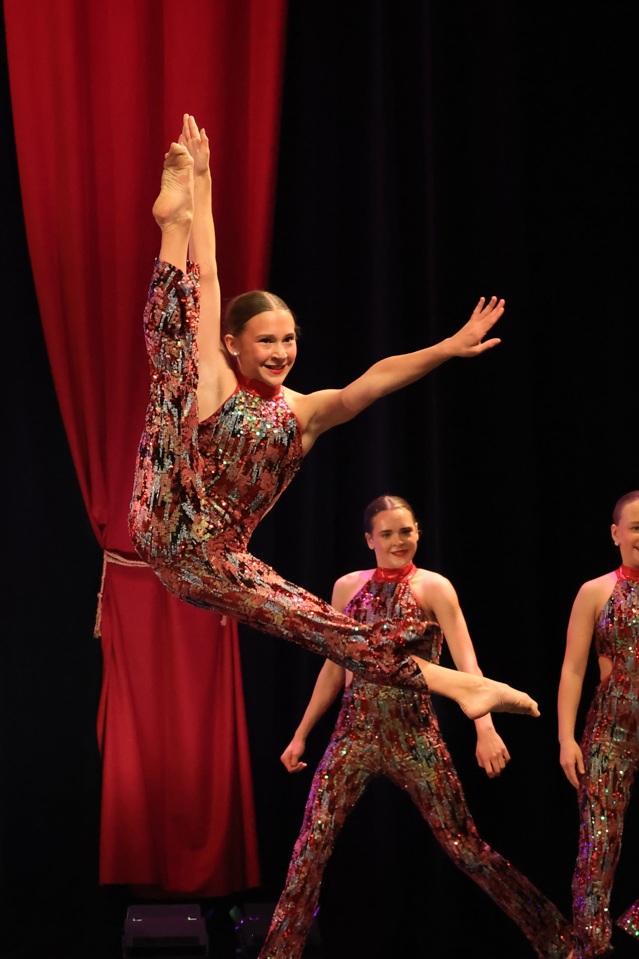 Dancer in a red sequin jumpsuit leaping mid-air during a jazz number