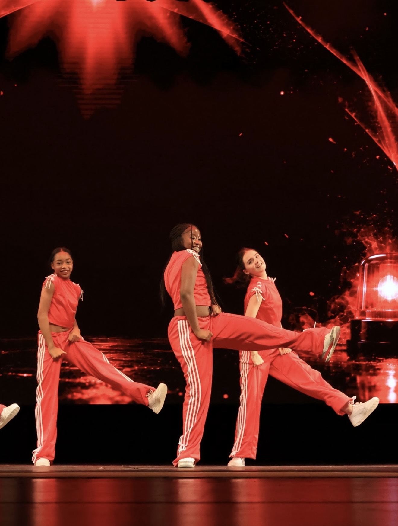 Three The Crew dancers in red outfits kicking in unison on stage