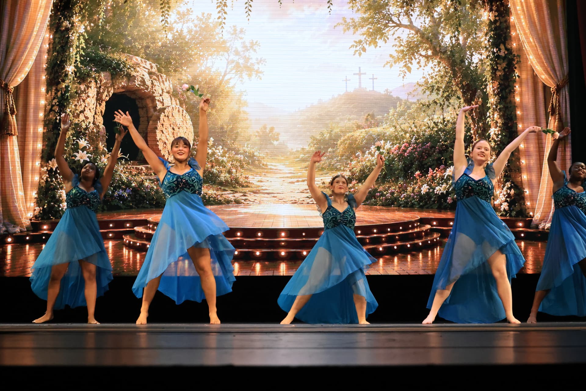 Dancers in flowing blue lyrical dresses performing in a garden scene